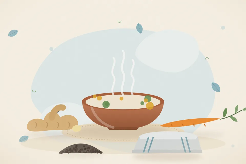 A bowl of thin golden soup with ginger slices and carrot pieces, and a few black peppercorns beside it on a kitchen table.