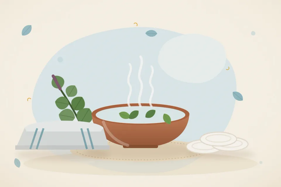 Warm folded cloth over a bowl of warm water, cotton pads and a sprig of tulsi on a pale blue background