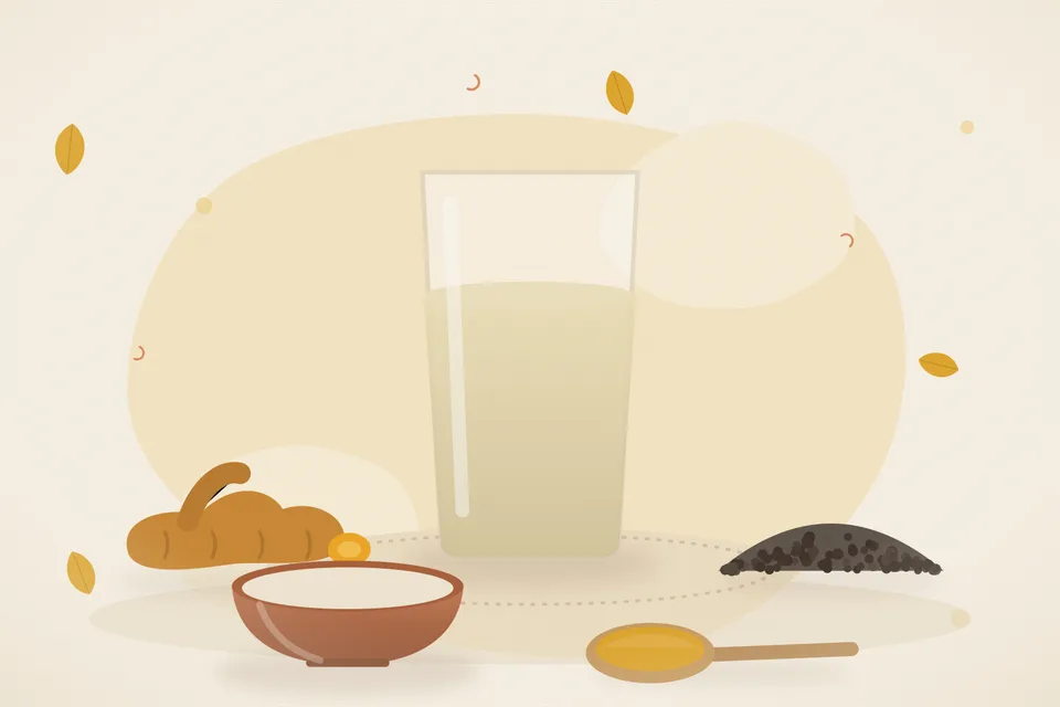 Turmeric powder, crushed black pepper and a brass tumbler of warm water on a wooden board